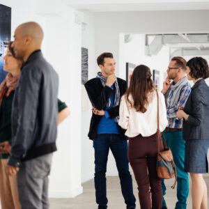 A group of people discussing art on display at an art exhibition in a gallery space