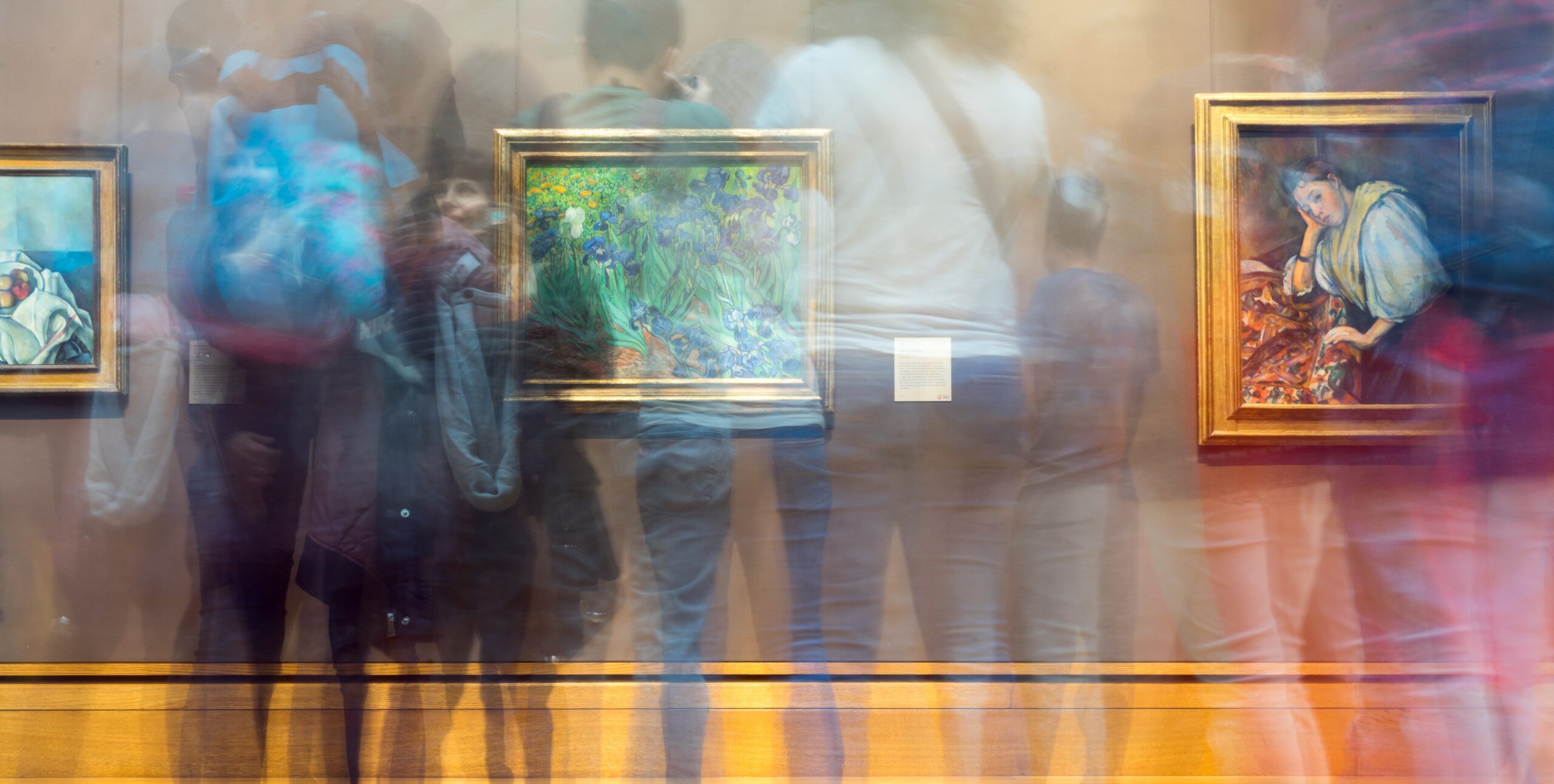 A busy art gallery showing lots of people looking at works on the wall.